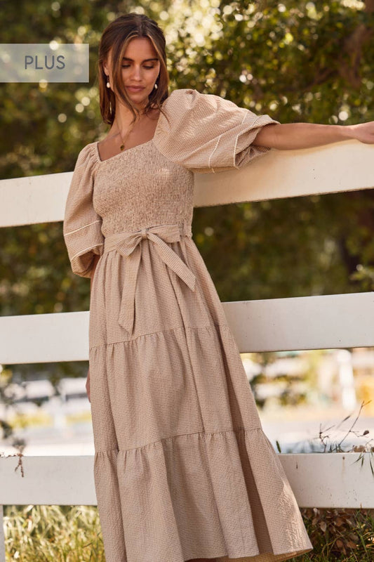 Woman wearing a beige dress with puffed sleeves standing by a white fence outdoors.